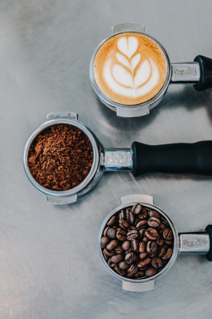 Espresso portafilters with latte art, coffee grounds, and roasted beans