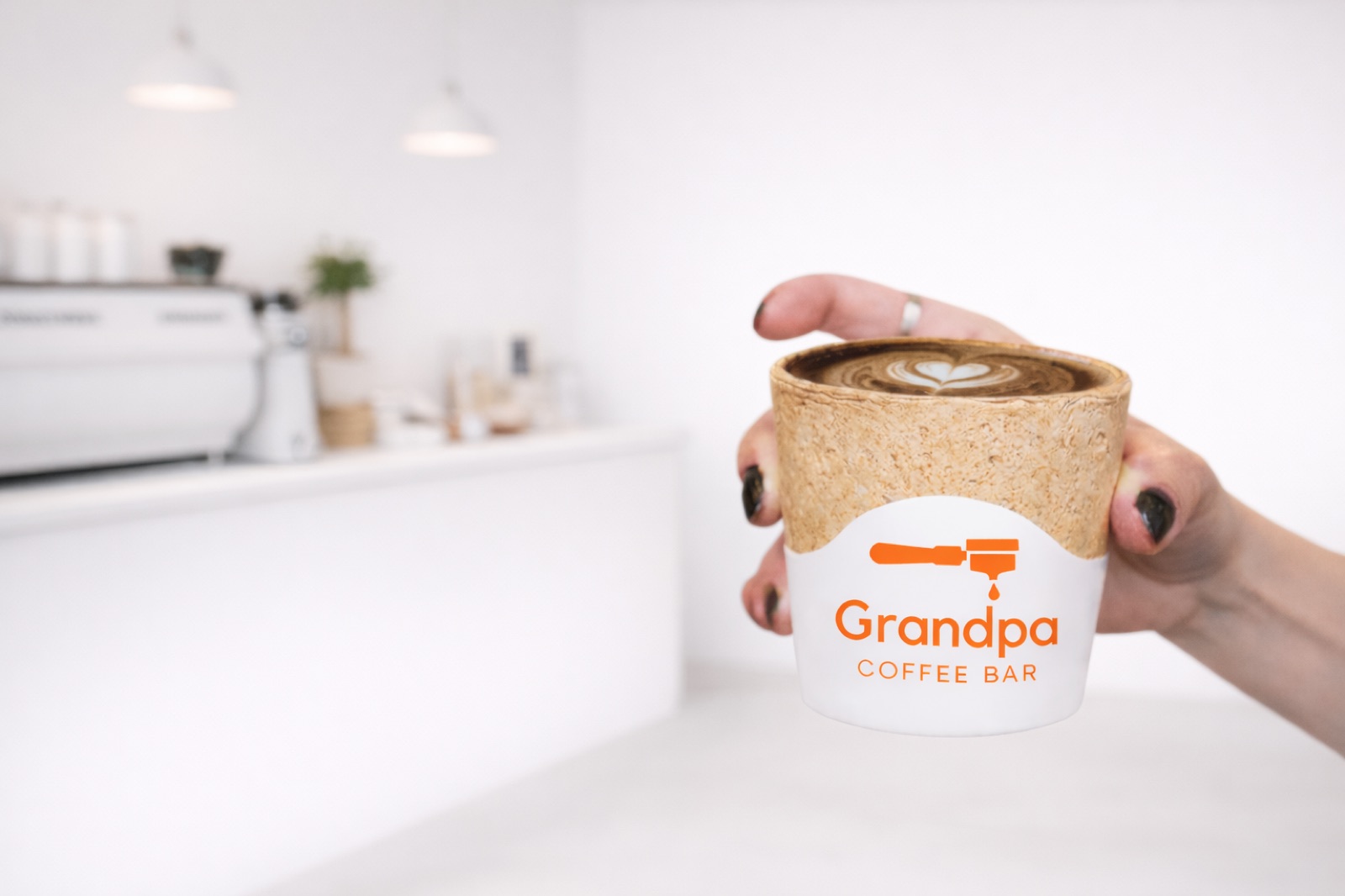 Hand holding a Grandpa Coffee Bar branded cup with latte art in a bright café